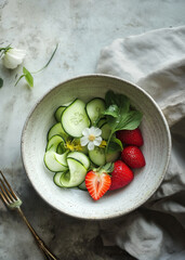 Fresh cucumber and strawberry salad with edible flowers in ceramic bowl