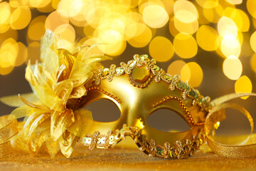 Beautiful carnival mask on golden shiny surface against blurred lights, closeup
