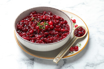 Tasty cranberry sauce in bowl, berries, thyme and spoon on white marble table, closeup