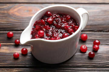 Tasty cranberry sauce in gravy boat and berries on wooden table, closeup