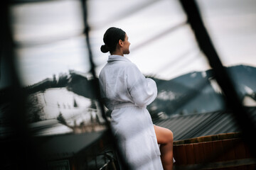 Woman in a white swimsuit relaxes in hot water with winter mountains in the background