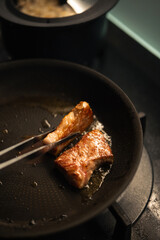 Seared Wagyu beef cube held with tongs over a sizzling black nonstick frying pan on a gas stove, capturing the rich marbling and golden crust.