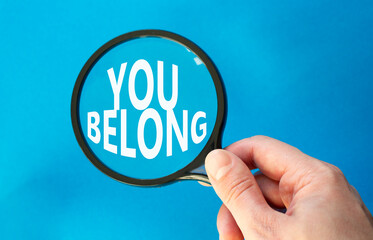 You belong symbol. Concept words You belong on magnifying glass. Beautiful blue background. Businessman hand. Business and You belong concept. Copy space.