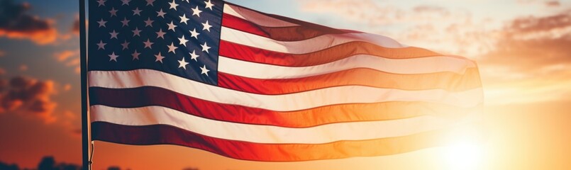 Fototapeta premium The American flag waves proudly against a backdrop of a stunning sunset, filling the sky with warm hues while illuminating the surrounding landscape.