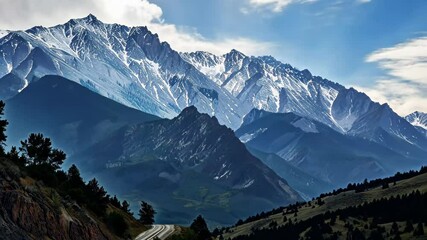 A stunning view of towering, snow-covered mountains contrasts with the verdant valleys below, reflecting the beauty of nature in early autumn under a clear blue sky.