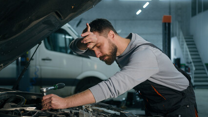 Caucasian mechanic in uniform repairing engine fixing motor inside open bonnet automobile...