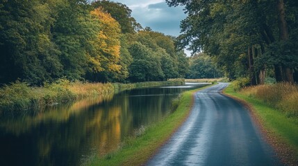 A quiet road beside a peaceful river, the calm waters reflecting the surrounding trees.