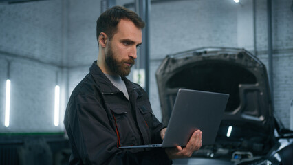Professional mechanic Caucasian man in uniform male industrial worker technical mechanical engineer using laptop check automobile diagnostics auto system engineering work car maintenance in service