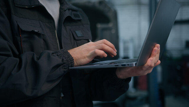Close up male hands use laptop computer diagnostics checking car in workshop auto repair service unknown man mechanic specialist engineer conducting diagnostics test search vehicle details on website