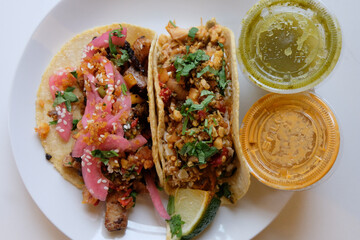 Overhead view of plated tacos with green and orange sauces, lime wedge, and fresh herbs