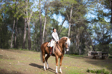 portrait of equestrian woman, young and beautiful, riding and holding the reins of her purebred brown horse with blond mane and tail. The woman is happy. Concept of love for the horse.