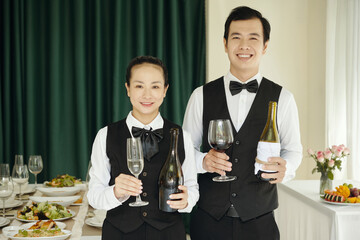 Portrait of colleagues in uniform standing with alcohol drinks and smiling at camera