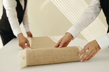 Close-up of waiters spreading decor cloth on dining table before setting it