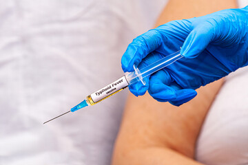 The picture shows a doctor holding a syringe with the typhoid fever vaccine in her hand, wearing...