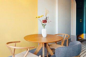 Close-up of a round wooden table with a vase of flowers. Stylish chairs in the dining room at home. Modern kitchen interior.