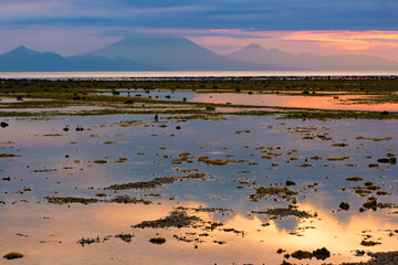 View of low tide of the Indian ocean and the outline of the island Bali and mount and volcano Gunung Agung from the beach of Gili Trawangan, Indonesia. Seascape at sunset. Reflection in water. 