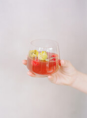 Refreshing cocktail served in a glass with edible flowers and cherries against a light background