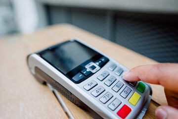 Finger touching contactless payment terminal on wooden surface, processing wireless banking transaction