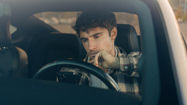 Displeased upset sad Caucasian man guy male driver car owner inside automobile on parking lot using mobile phone problem with smartphone read bad news frustrated anxious millennial driving auto city