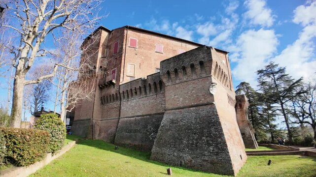 Medieval fortress of Dozza castle rising majestically on a green hill in Emilia Romagna, Italy, showcasing its brick walls and defensive structures against a blue sky