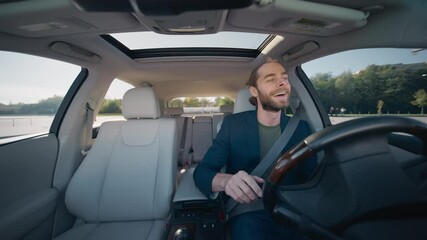 Caucasian man sitting behind steering wheel while driving in automobile. Moving hand in rhythm of music playing on radio. Singing song with wide smile. Way to work or home. Transportation concept.