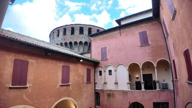 Internal courtyard of Dozza castle with arches, columns, plants and red windows, creating a picturesque and historic atmosphere in Emilia Romagna, Italy