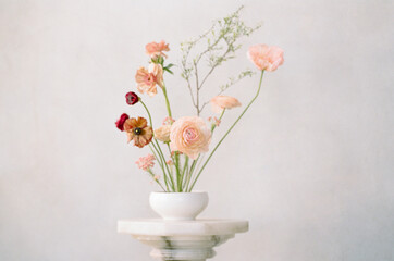 Elegant floral arrangement with soft pastel colors displayed in a white vase on a simple pedestal