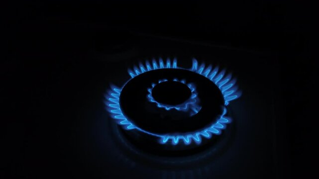 Slow motion close-up of a gas stove burner igniting with blue flame