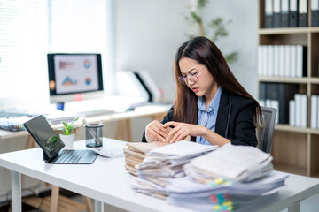 A woman is sitting at a desk with a pile of papers in front of her