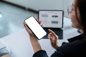A woman is holding a phone and pointing at a laptop screen