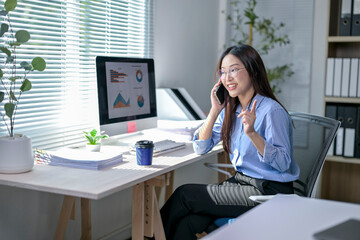 A woman is sitting at a desk with a computer monitor and a cell phone