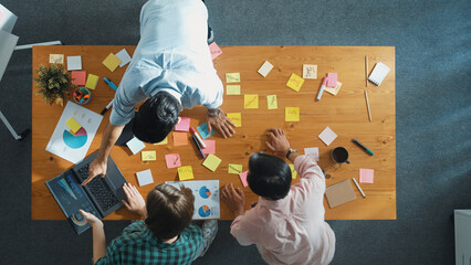 Top view of skilled manager using laptop while team support her work. Caucasian female leader working and planning creative start up project with colleague at meeting table with notes. Convocation.