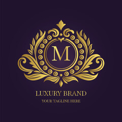 Gold Letter 'M' Logo with Ornamental Patterns and Floral Motifs on Purple  
