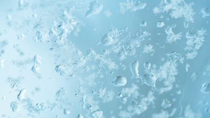 Close up of a delicate snowflakes melting on a wet, blue glass surface during a serene winter day, capturing the ephemeral beauty of nature's frozen artistry