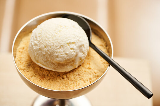 A scoop of rich vanilla ice cream rests on a generous layer of cookie crumbs inside a sleek metal bowl. The dessert looks tempting, ready to be savored and enjoyed