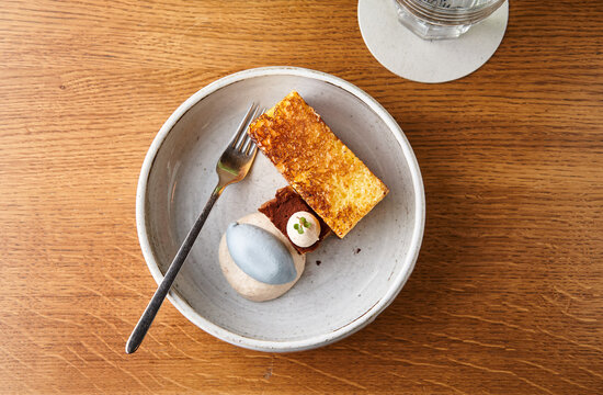 A rustic plate holds an assortment of desserts, including a golden cake, chocolate treat, and a unique round dessert, accompanied by a fork and a glass of water