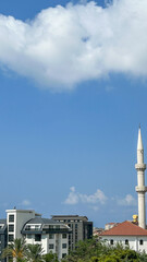 White Minaret Tower Above A Modern Cityscape With A Clear Blue Sky, Alanya, Turkey, Representing Islamic Architecture, Religious Heritage, Travel, And Urban Development.