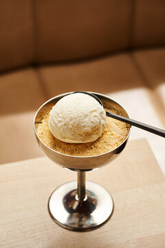 A creamy scoop of vanilla ice cream rests on a bed of crumbled cookies in a shiny silver dish. The dessert is illuminated by soft natural light, creating an inviting atmosphere