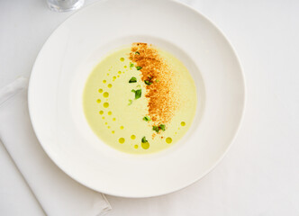 A green vegetable soup is artistically arranged on a white plate, showcasing vibrant green herbs and a sprinkle of spices. Perfect for elegant dining experiences or gourmet events