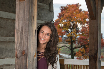 Cute young brunette woman poses for photo near log cabin