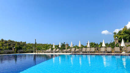 A Luxury Resort Pool With Blue Water, Sun Loungers, And White Umbrellas In Alanya, Turkey, Under A Clear Sky, Representing Relaxation, Travel, And Hospitality For Tourism And Real Estate.