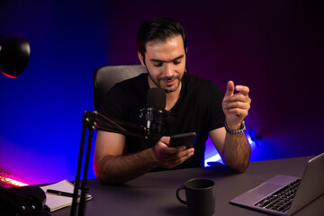 Broadcaster talking to listener on live streaming online, checking message from smartphone on...