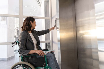 Businesswoman in wheelchair in corporate office using touch panel to operate the lift © zinkevych