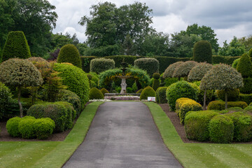 A garden with hedges and a statue of a woman. The garden is well-maintained and has a peaceful atmosphere