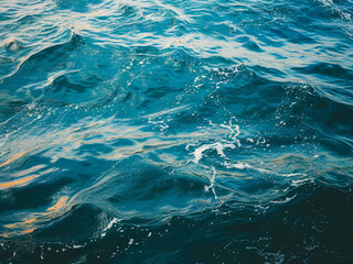 Fototapeta premium Close-up of the ocean's surface under a cloudy sky, featuring deep gray-blue waves with silvery reflections. White foam accents the dynamic water, blending shadowed depths