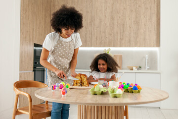 African American mother and daughter celebrate Easter and paint eggs with farbe and brush at home, woman with child decorate Easter eggs
