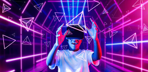 Smart teenager wearing VR glasses and excited about geometric shape. African gamer wearing casual cloth and surrounded with glowing light color while using augmented reality technology. Ingenuity.