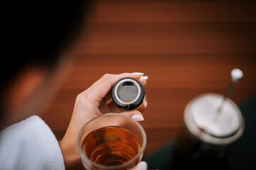 Woman in white robe enjoying tea on terrace with snow-capped mountains in the background during a quiet morning