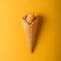 Waffle cone filled with waffle pieces on a vibrant yellow background. Creative food and summer concept.
