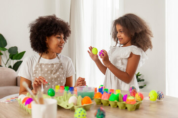 African American mother and daughter celebrate Easter and paint eggs with farbe and brush at home, woman with child decorate Easter eggs